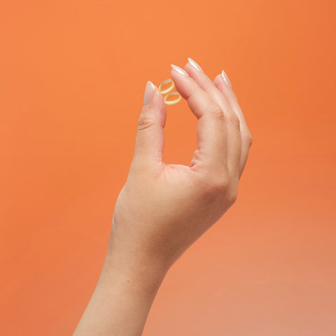 Lifestyle image of a hand holding CBD capsules, orange and pink background