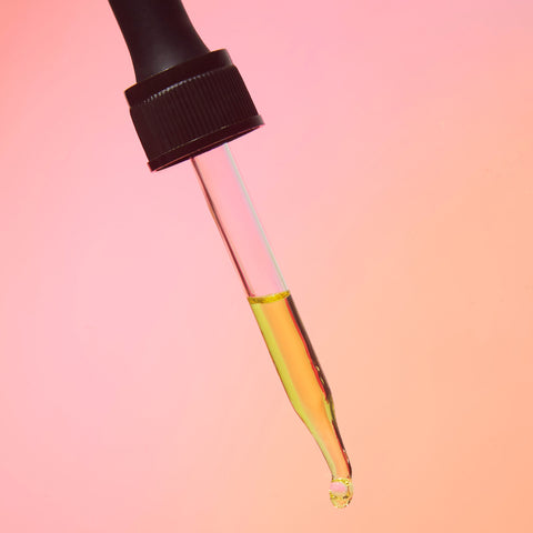 Lifestyle image of a tincture dropper, orange and pink background