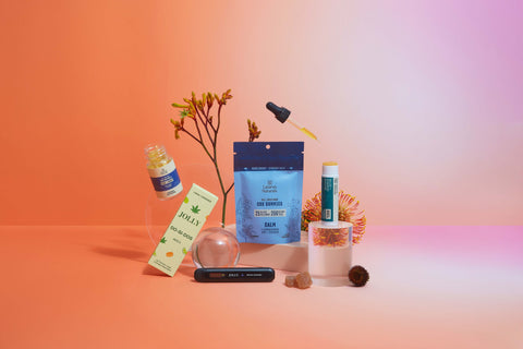 Lifestyle image of CBD products and plants on a table, orange and pink background
