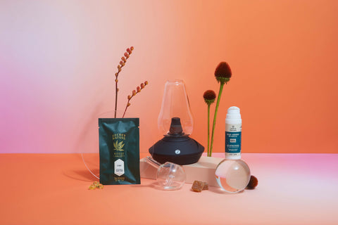 Lifestyle image of a variety of CBD offerings and accessories on a table. Orange and Pink Color.
