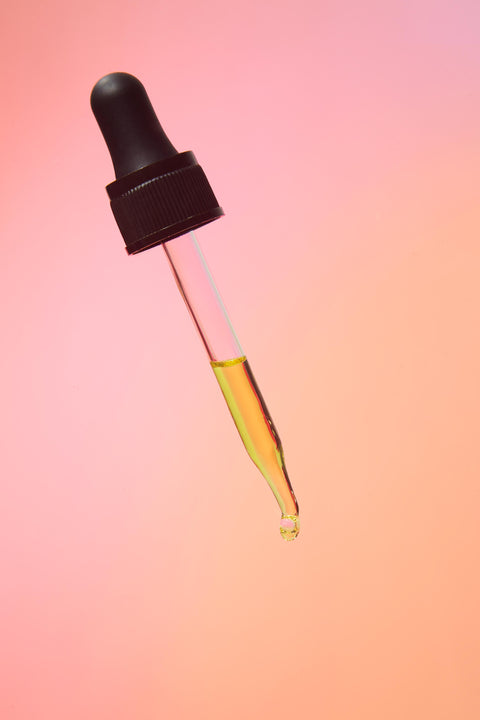 Lifestyle image of a tincture dropper, orange and pink background