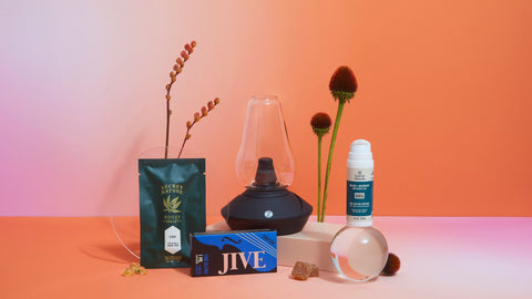 Lifestyle image of CBD products and accessories on a table, orange and pink background