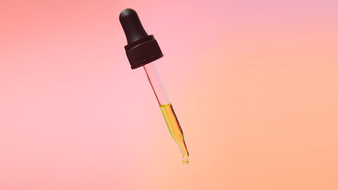Lifestyle image of a tincture dropper. pink/orange background